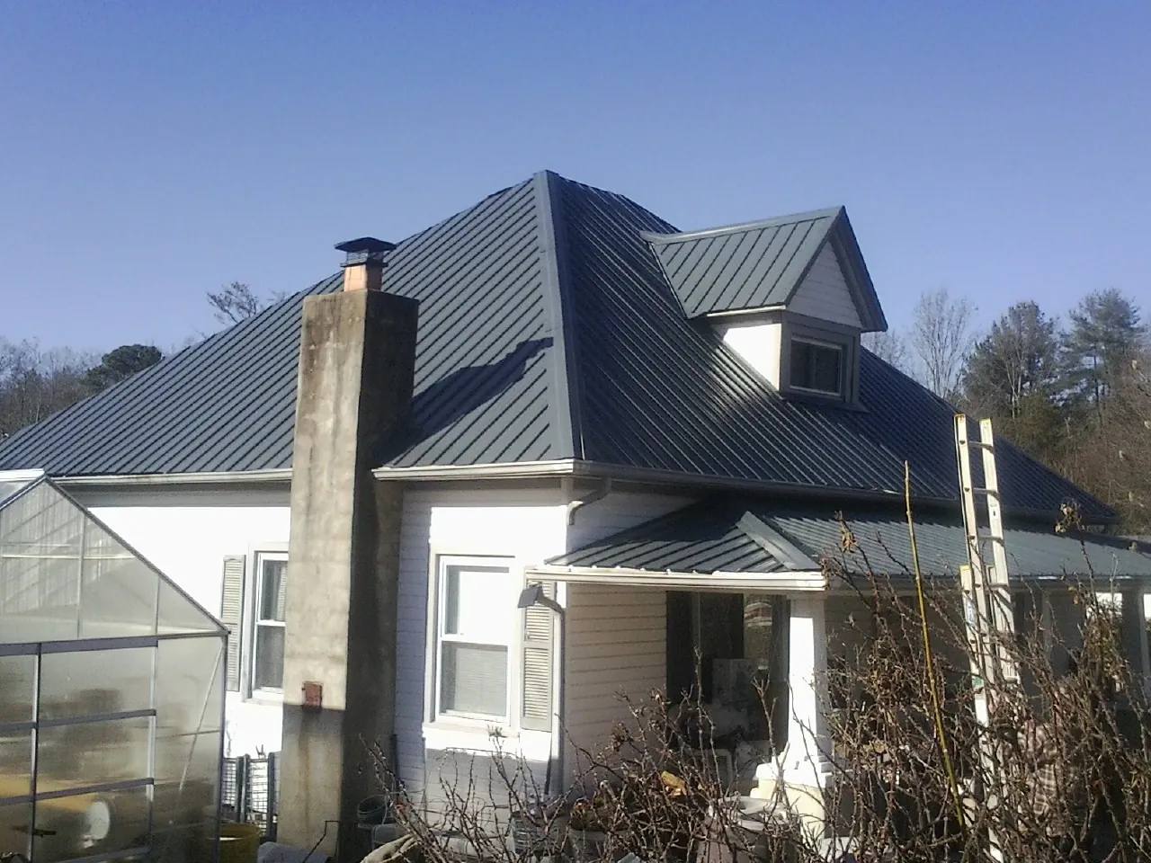 Dark blue standing seam metal roof on a white farmhouse with dormer — Slate & Tile Roof Repair by Roofing Brothers in Winner