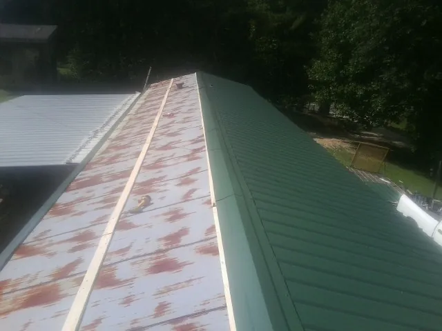 Old rusted panels beside newly installed green metal roofing — Wind Damage Roof Repair by Roofing Brothers in Winner