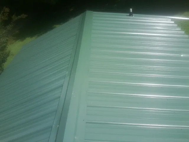 New green metal panels meeting at the ridge of a roof — Flat Roof Repair work by our crew in Winner
