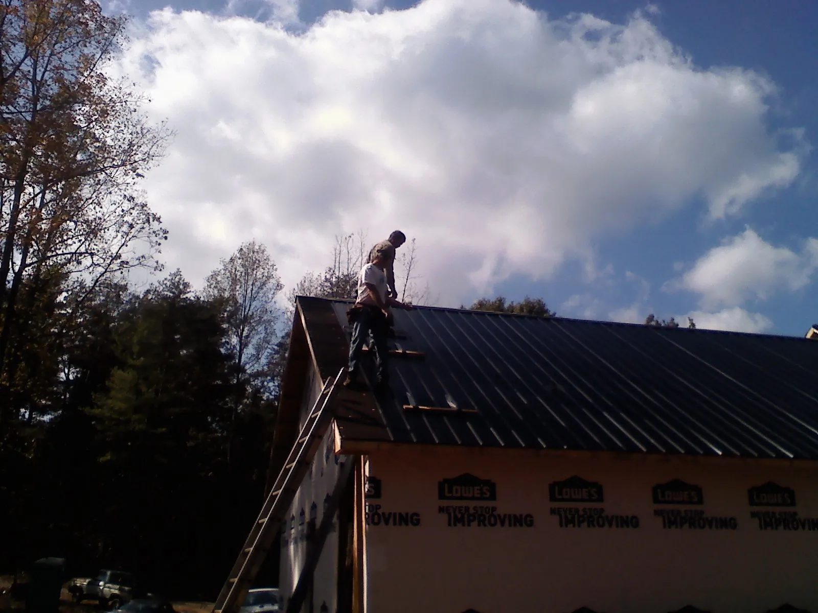 Roofer fastening dark metal panels high against a cloudy sky, from a Roof Inspection job in Winner