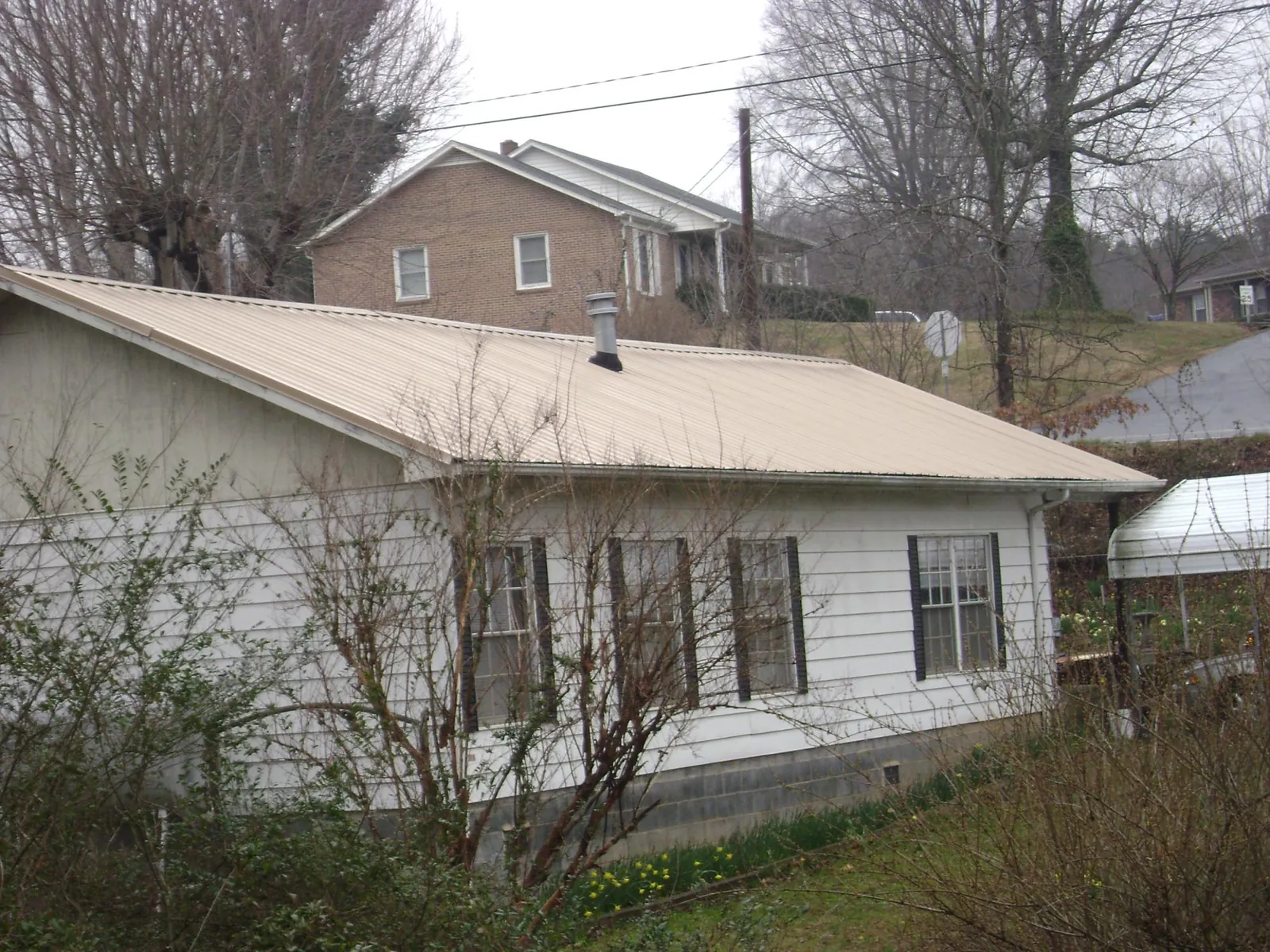 Tan metal roof on a white sided house set into a hillside — Commercial Roofing by Roofing Brothers in Winner